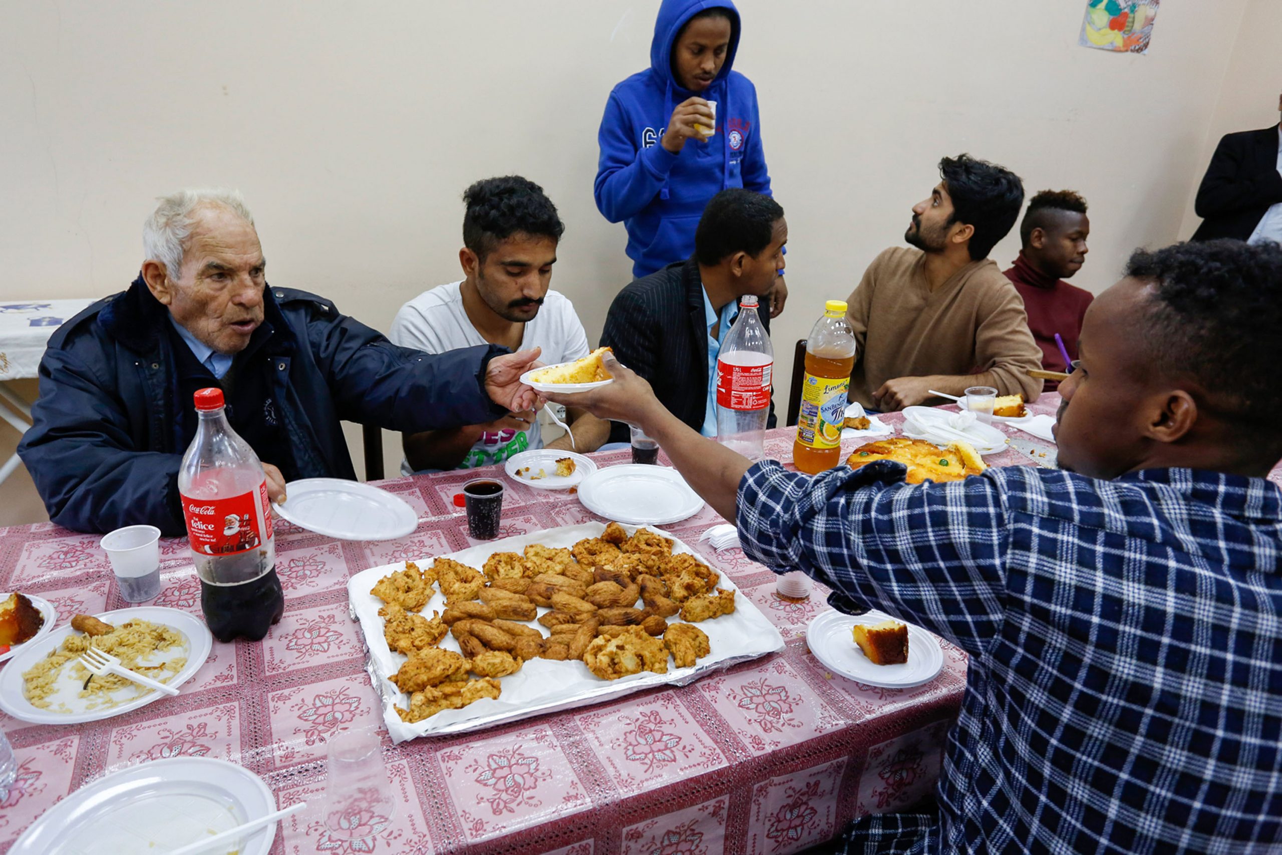 Local residents join refugees for a meal at the Palazzo Condo, a hostel for refugees in Satriano, Italy, on Monday, Feb. 15, 2016. XXX INSERT SECOND SENTENCE HERE XXX Photographer: Luke MacGregor/Bloomberg